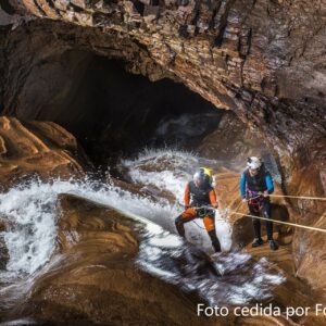 Dos personas haciendo espeleobarranquismo en una cascada dentro de una cueva