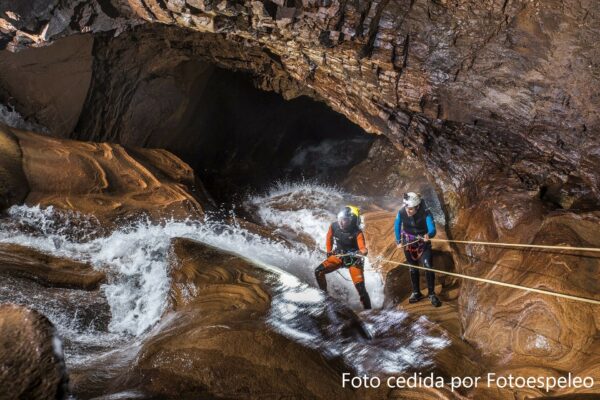 Dos personas haciendo espeleobarranquismo en una cascada dentro de una cueva